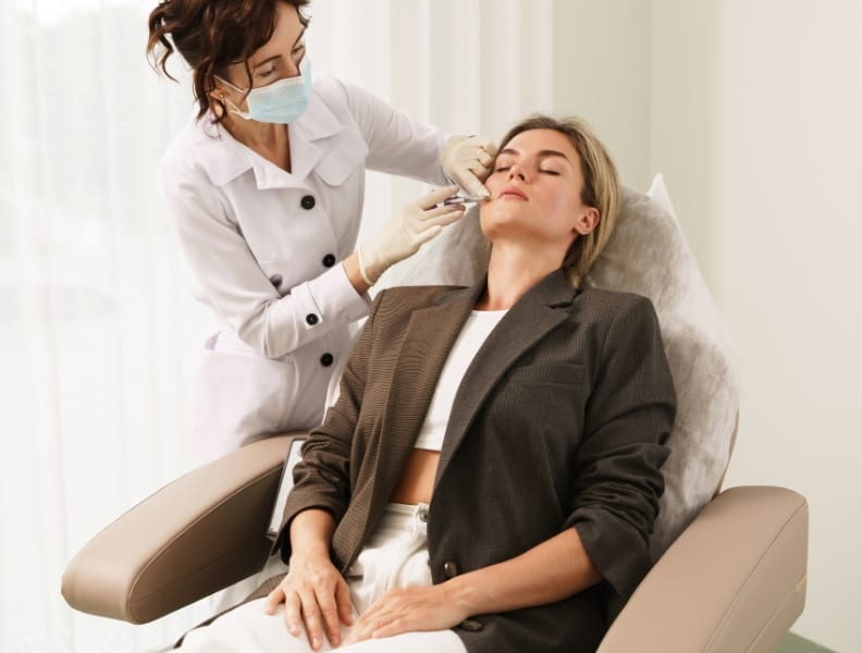Photograph of models: an aesthetic provider in a mask treats a relaxed patient seated in a treatment chair