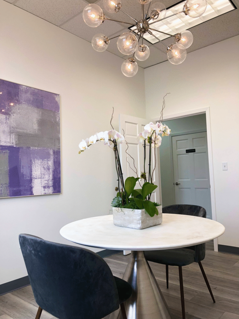 Small room with a round white table, an orchid centrepiece and dark upholstered chairs