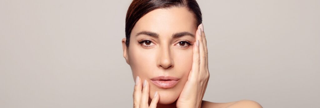 Photograph of a model: a woman with clear skin holds both hands at her face